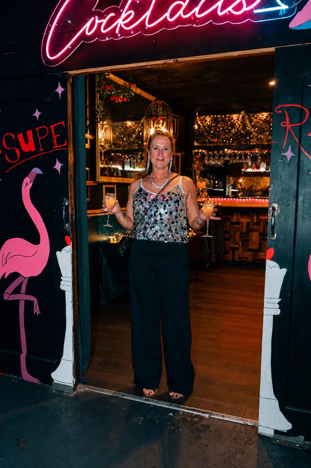 Guest with two cocktails in the Cocktail Lounge doorway under the neon Cocktails sign