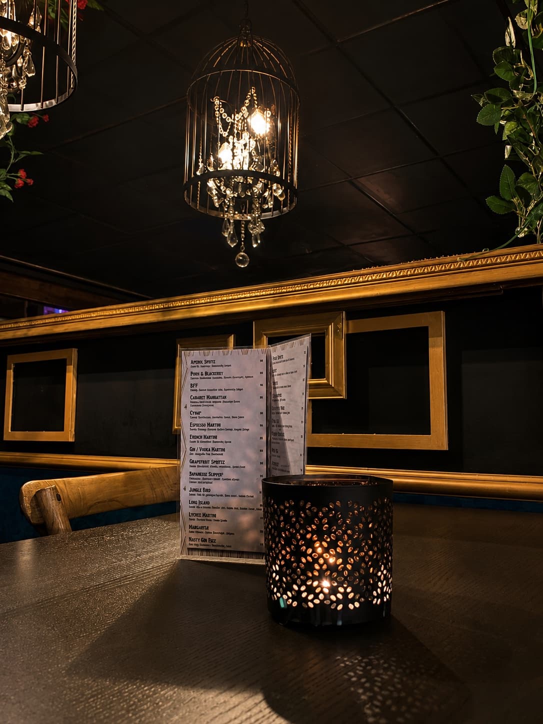 Cocktail menu and a lit tealight on a table beneath the birdcage chandelier