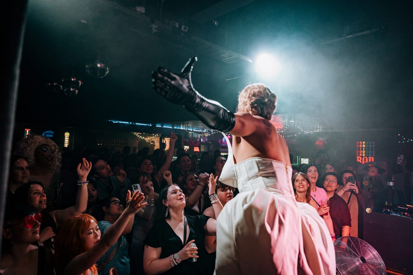 Drag performer in a white gown under stage lights at Pride