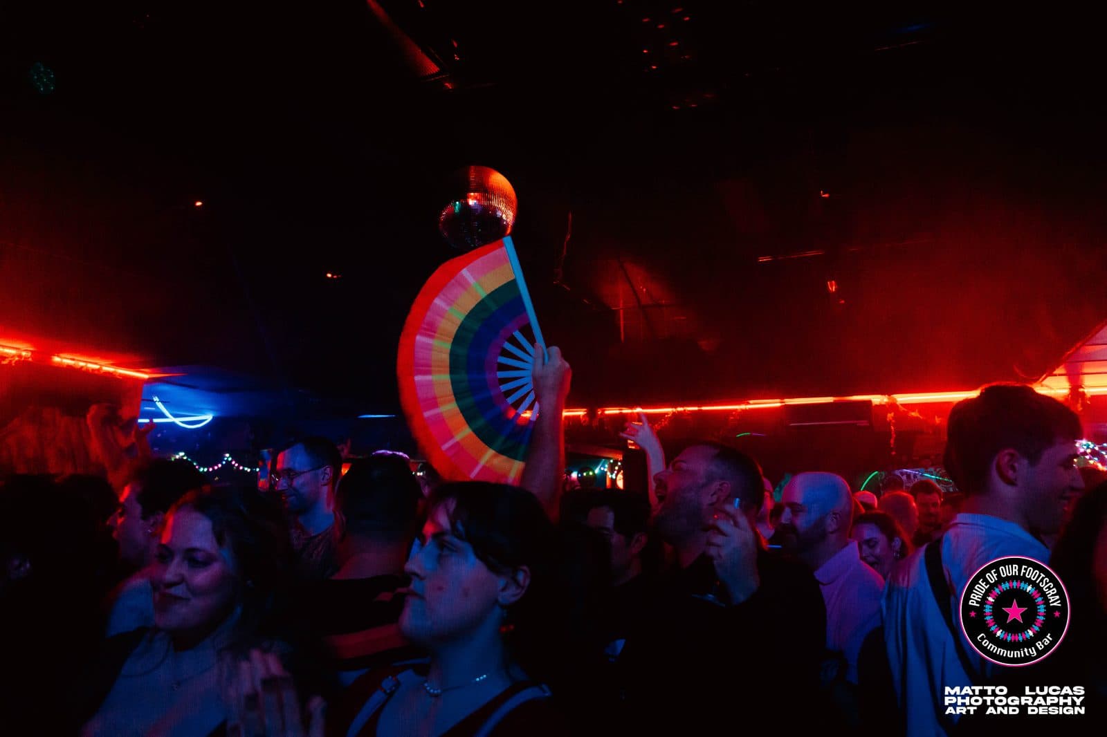 Rainbow hand fan raised above the dancefloor crowd, under the disco ball at Pride of our Footscray